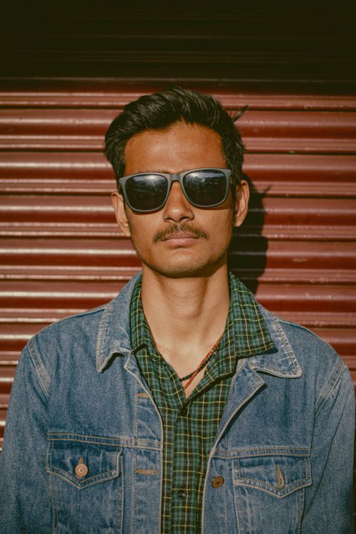 Free Portrait of a stylish man wearing sunglasses and denim jacket against a rolling door backdrop. Stock Photo