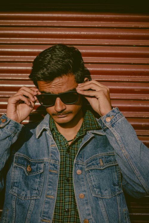Free Fashionable young man in a denim jacket adjusting sunglasses outdoors. Stock Photo