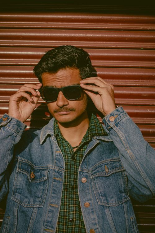Free A fashionable man in sunglasses and denim jacket poses confidently against a textured background. Stock Photo