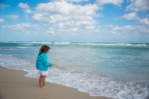 Free A young girl enjoying leisure time on a peaceful beach, touching the surf. Stock Photo