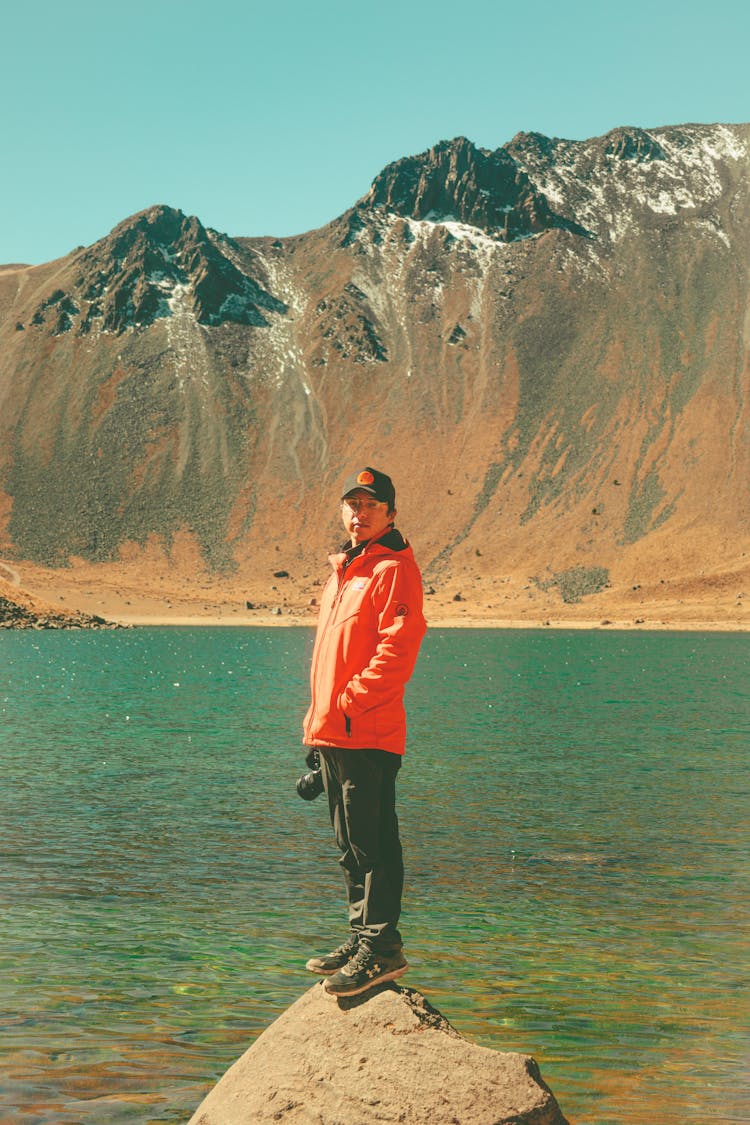 Man In Jacket Standing On Rock Over Lake