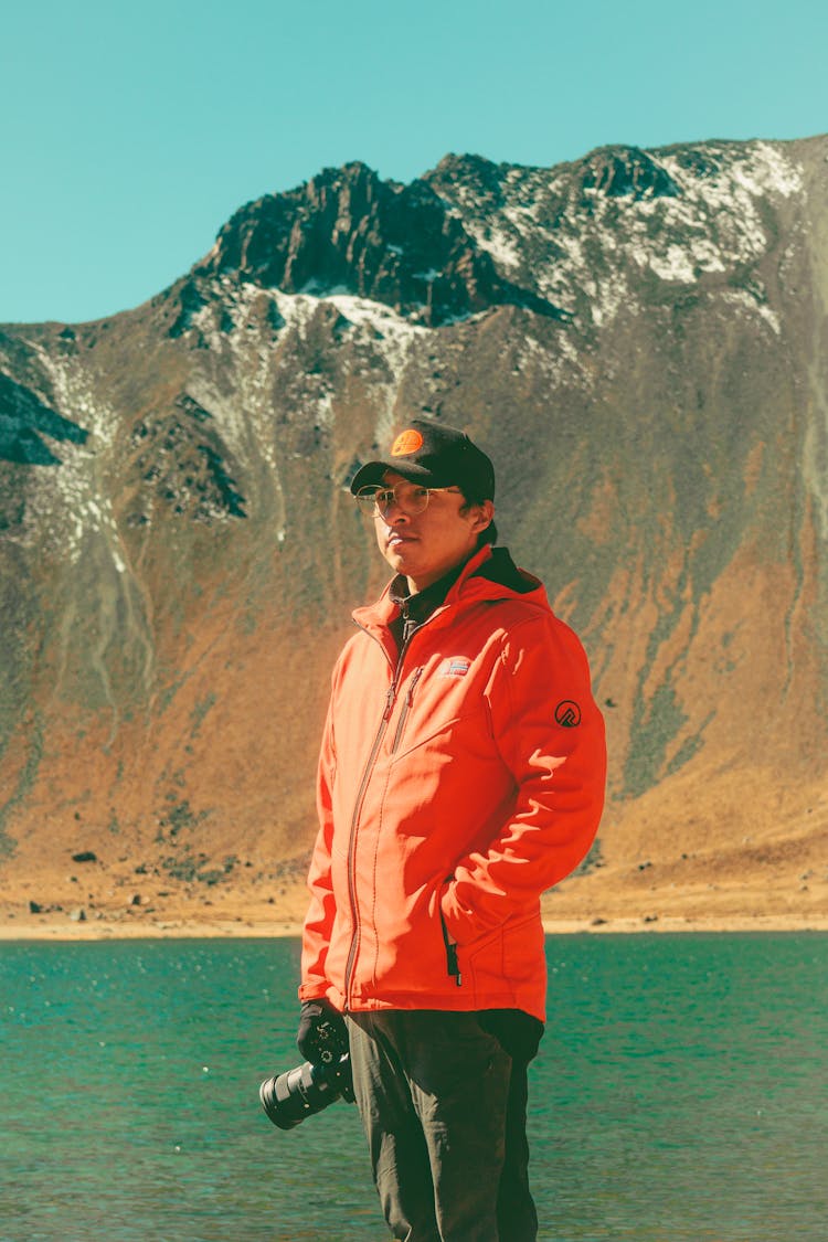 A Man Standing With A Camera By A Lake