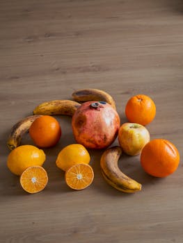 An arrangement of various fruits including bananas, oranges, lemons, and a pomegranate on a wooden table.