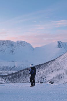 A solitary hiker enjoys a snow-covered mountain landscape at dusk.