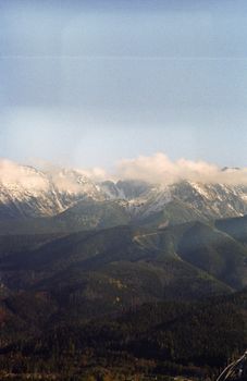 Breathtaking view of snowcapped mountains and lush green forests under a clear sky.