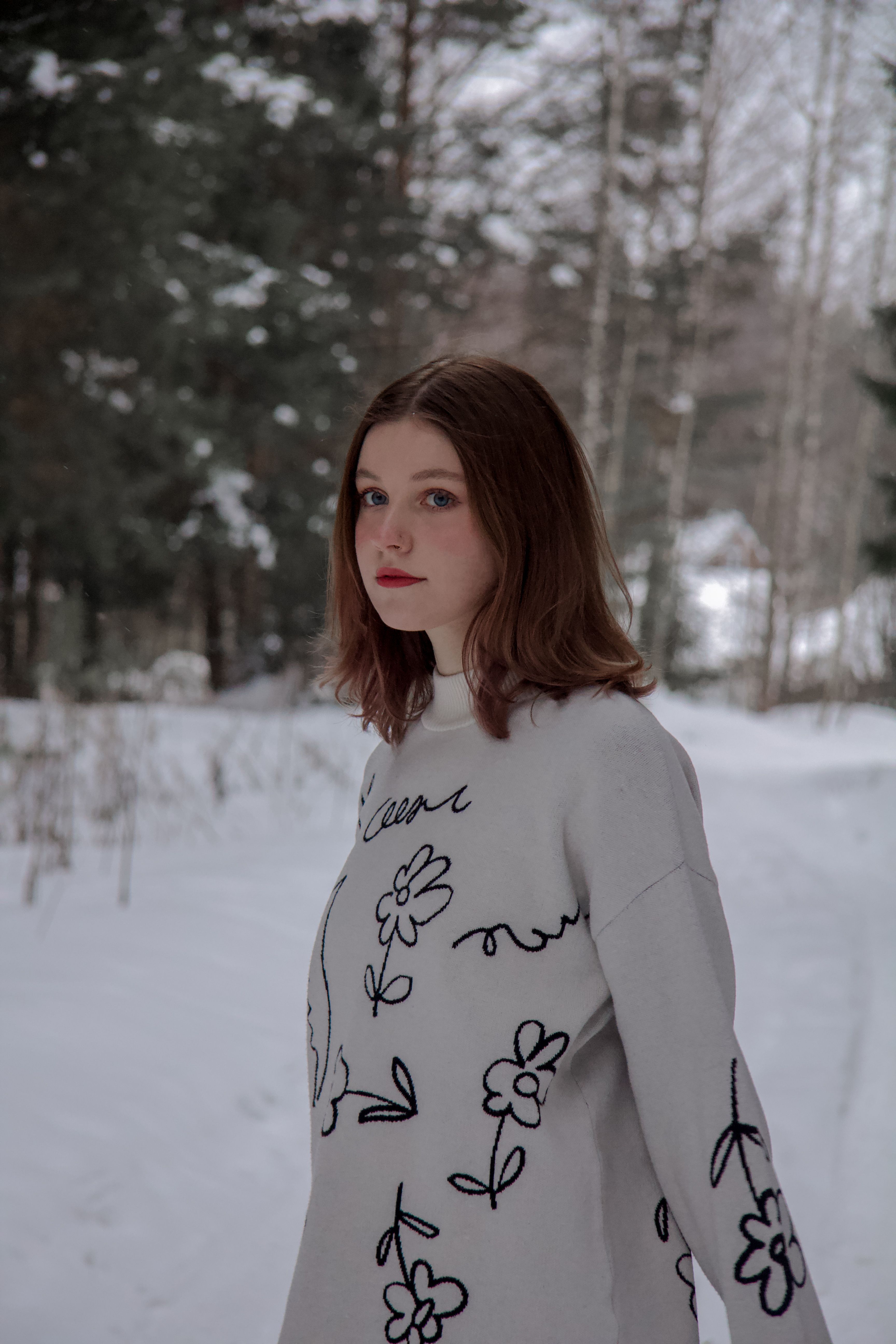 Portrait of a woman in a floral patterned dress in a snowy forest setting.