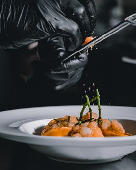 Close-up of chef's gloved hands seasoning a gourmet seafood dish in a restaurant kitchen.
