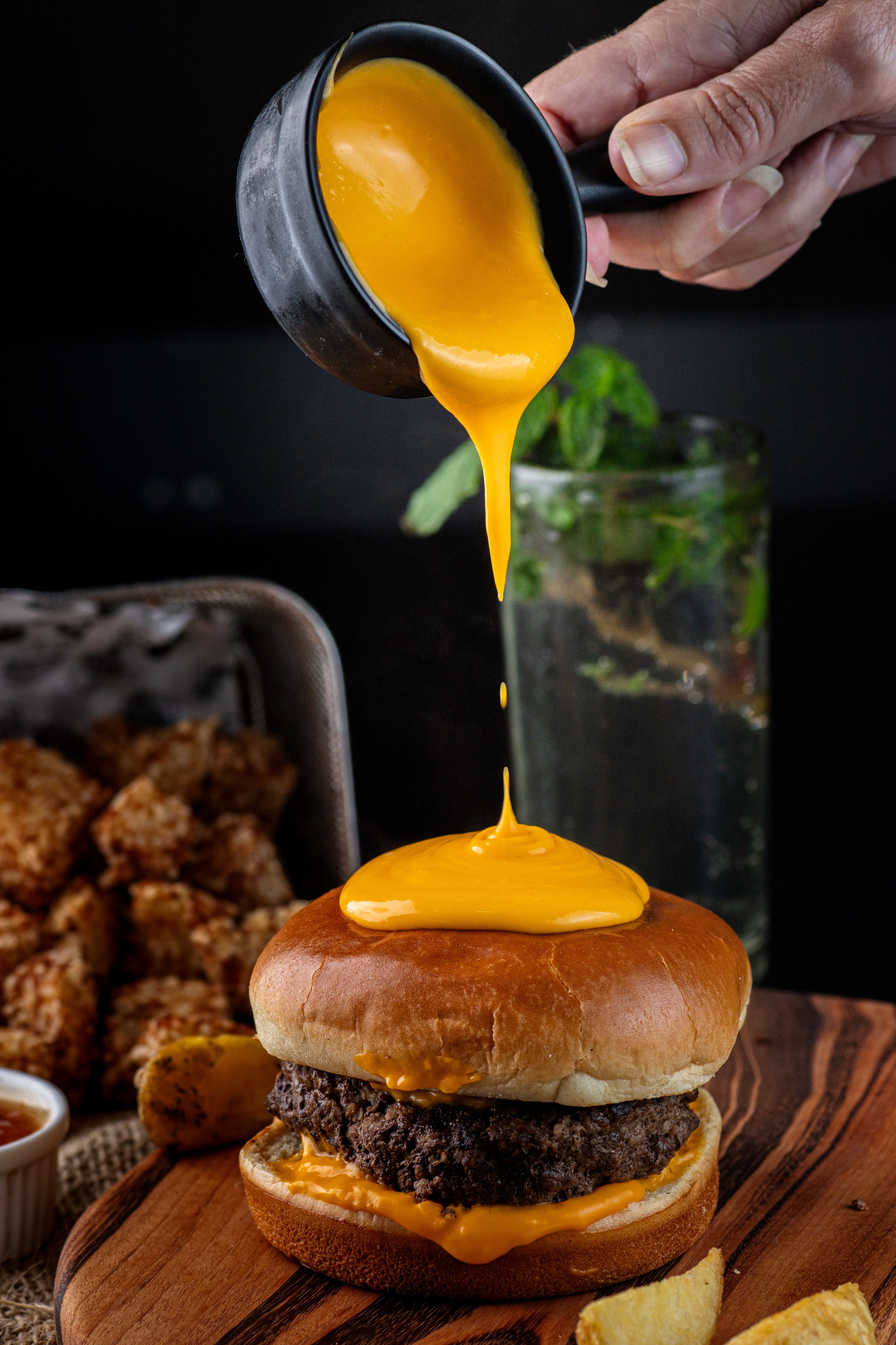 Delicious gourmet cheeseburger with cheese sauce being poured on top for a perfect fast food meal.