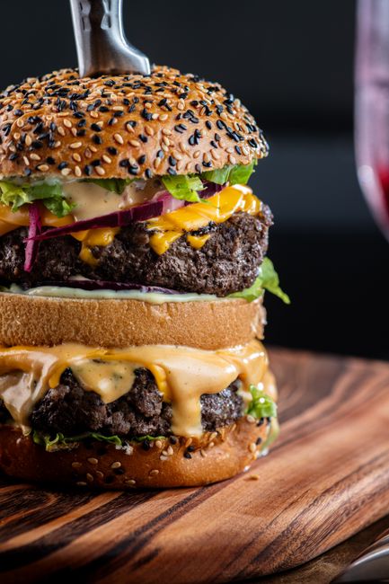 A stacked double cheeseburger with two thin beef patties, melted American cheese, grilled onions, lettuce, and tomato, oozing pink special sauce onto a toasted sesame bun.