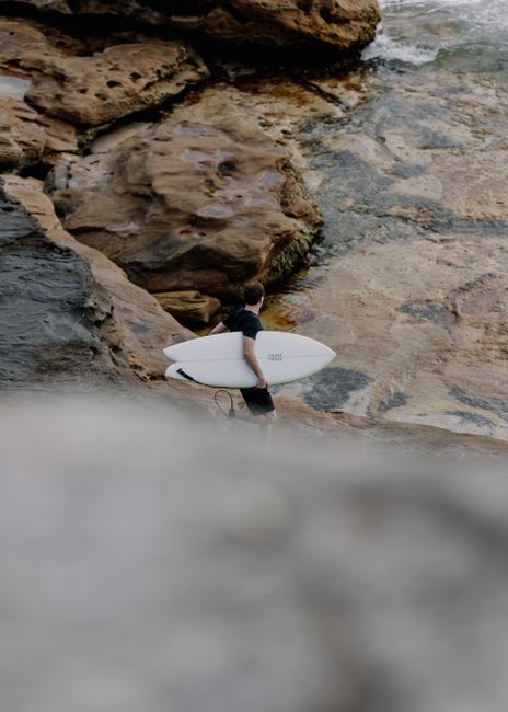 A surfer with a board standing on rocky cliffs at Bondi Beach, Australia, ready to hit the waves.