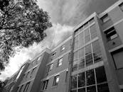 一张现代公寓建筑立面的低角度黑白照片，映衬着树木和天空