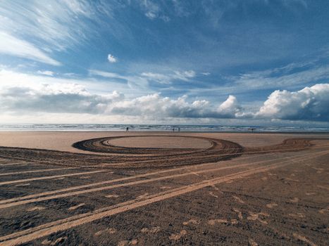 Peaceful beach scene at Praia Grande with vast sky and tire tracks on sand.