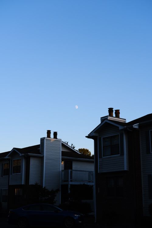 Free Serene suburban neighborhood with houses silhouetted against a clear, moonlit evening sky. Stock Photo