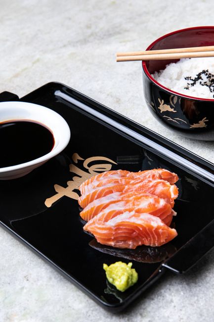 A small glass bowl of amber ponzu sauce next to halved yuzu and lemon, with a spoon resting on the rim.