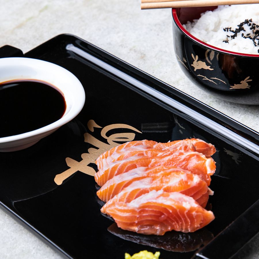 A close-up of salmon sashimi served with rice and soy sauce, showcasing Japanese cuisine.