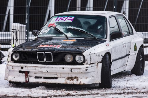 Free A worn race car parked on a snowy track, showcasing its rugged charm and racing stickers. Stock Photo