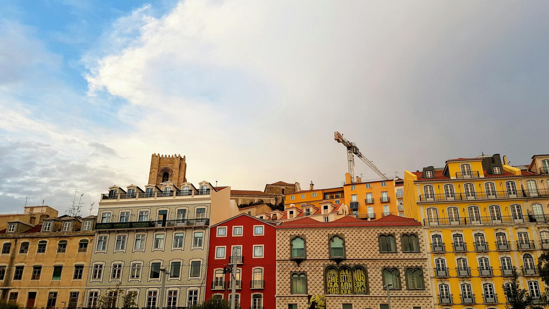 A vibrant view of Lisbon's historic R. Augusta with colorful buildings and a crane under a cloudy sky.