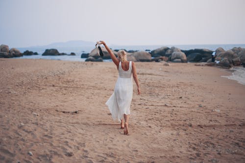 Free Woman Walking on the Beach with Shoes in Hands  Stock Photo