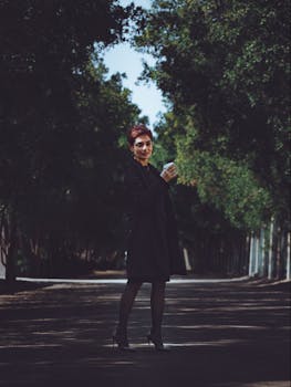 Woman in heels walking on a serene tree-lined street holding a coffee cup.
