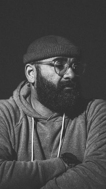 Black and white portrait of a bearded man wearing eyeglasses and a hoodie.