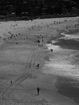A black and white scenic view capturing Bondi Beach's shoreline with people and waves.