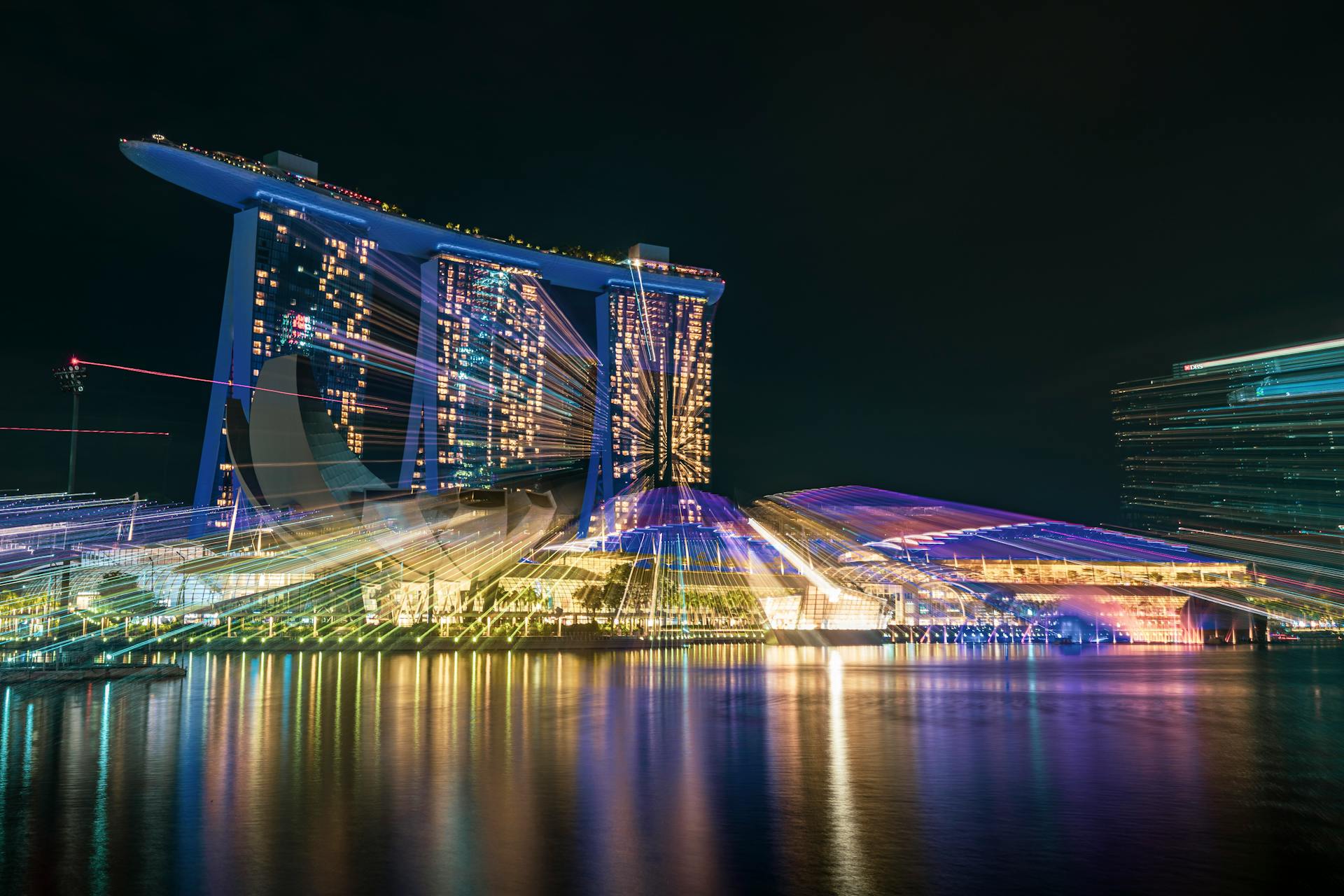 Vibrant night view of Marina Bay Sands in Singapore with dynamic light trails reflecting on water.