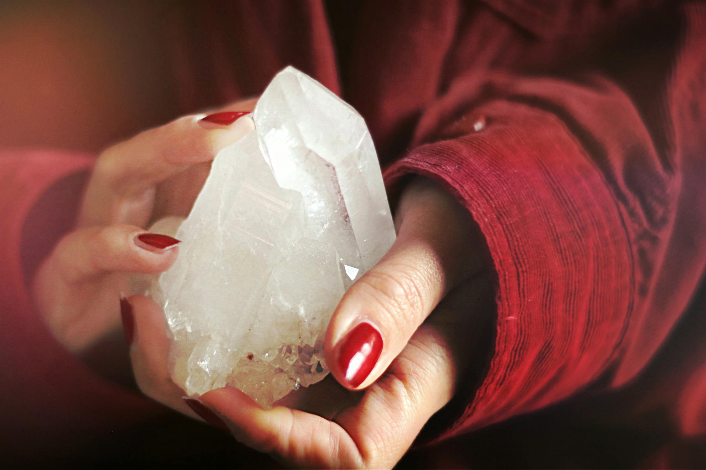 Woman in red jacket with red fingernails holding a white crystal. 