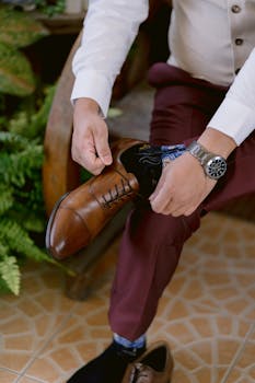 Close-up of a man tying a brown leather dress shoe, showcasing stylish menswear and attention to detail.
