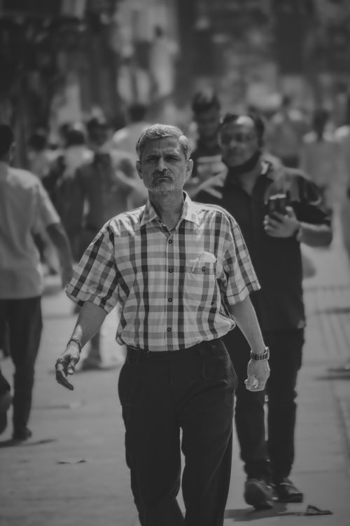 Free A candid capture of an elderly man walking down a busy city street in black and white. Stock Photo