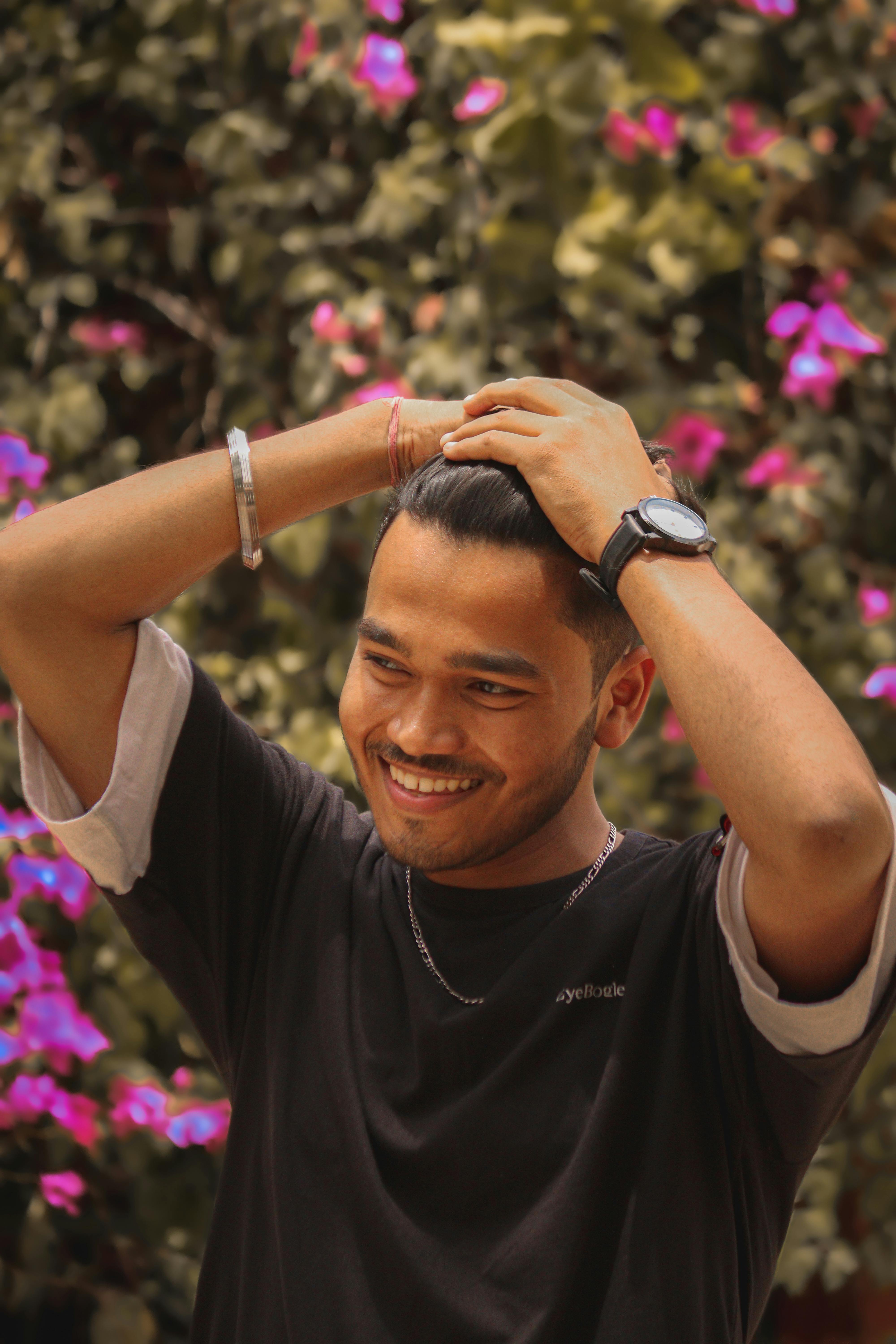 Young man smiles joyfully with vibrant flowers in the background, creating a lively summer mood.
