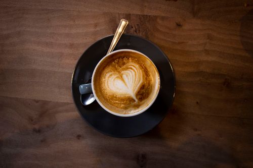 Free A latte with heart-shaped art served in a black saucer on a wooden table. Stock Photo