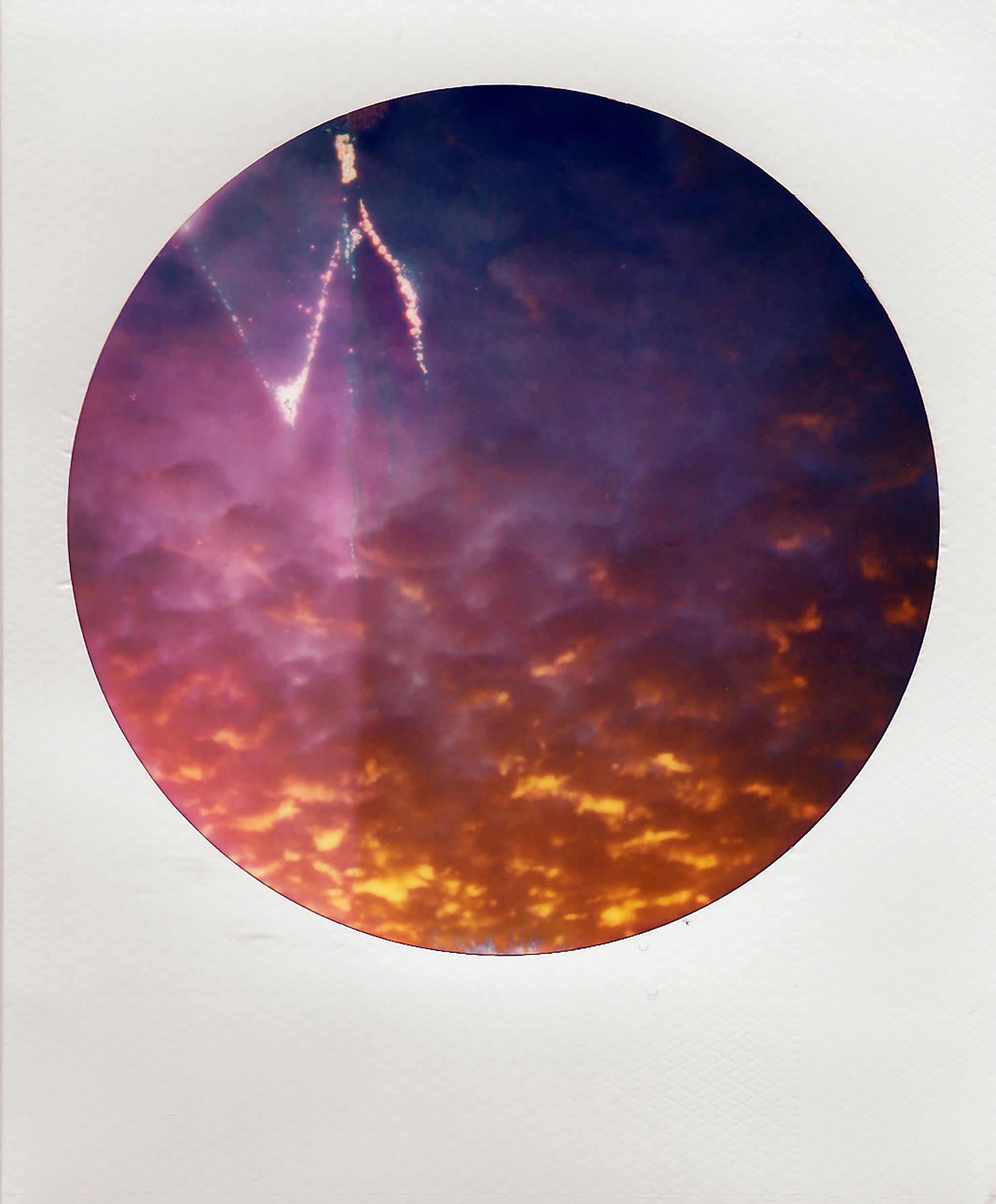 A colorful sunset captured in a unique circular Polaroid picture with vivid sky colors.