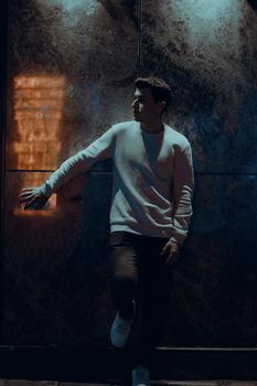 Young man posing stylishly against an urban backdrop at night, exuding mystery and charm.