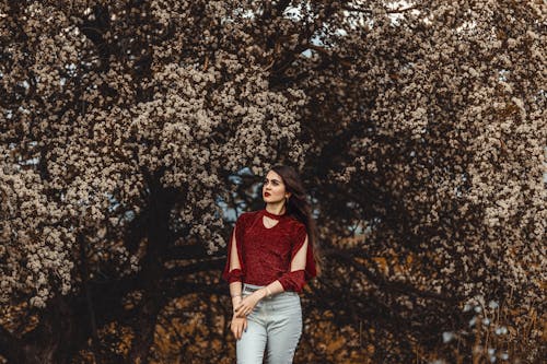 Young Brunette in Red Blouse Posing under Blossoms