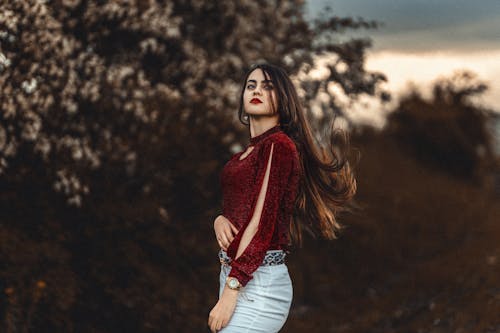 Young Brunette Wearing a Red Blouse and Red Lipstick Posing in a Park 