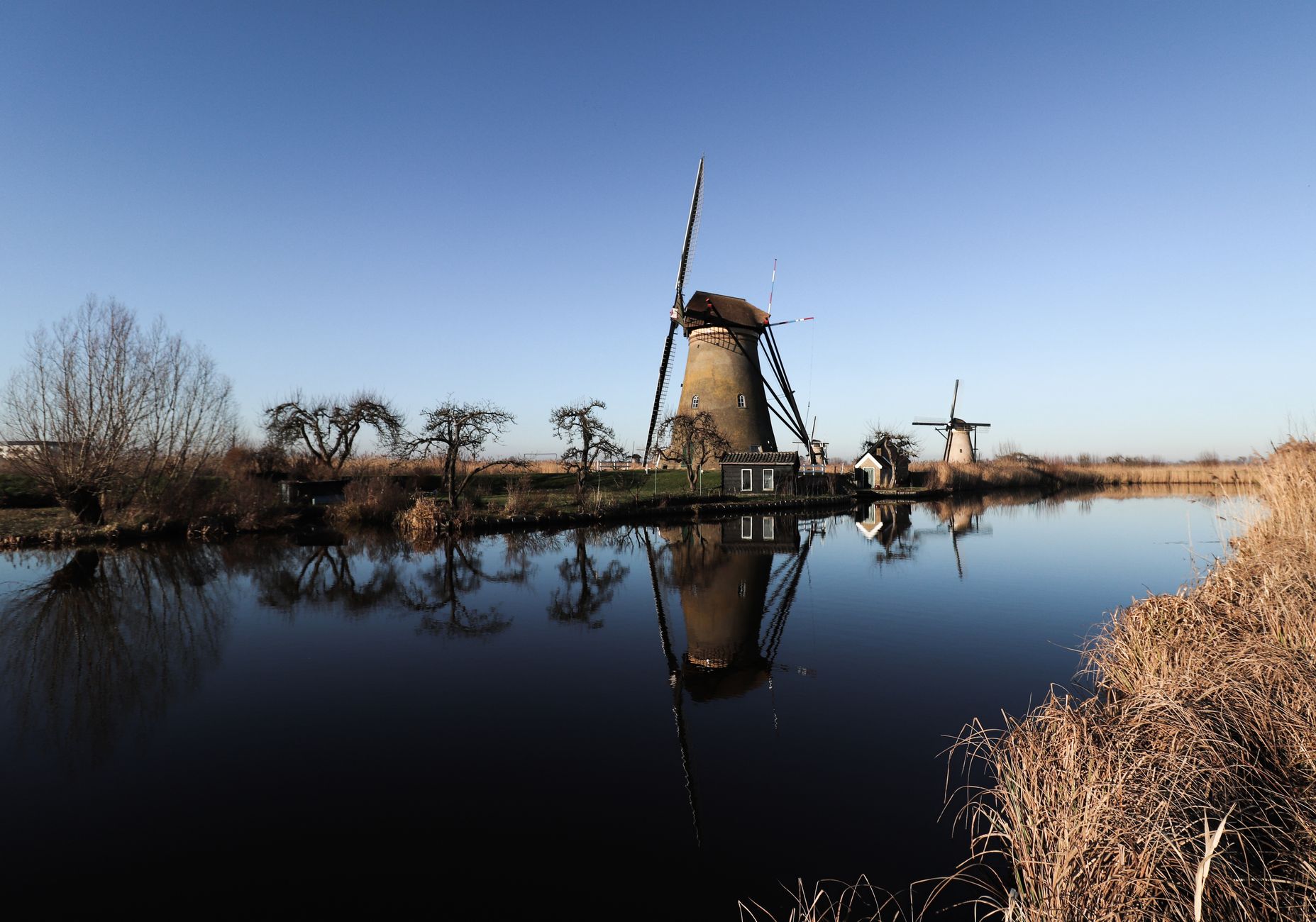 Historic Kinderdijk windmills with reflective river in clear skies, showcasing Dutch heritage.