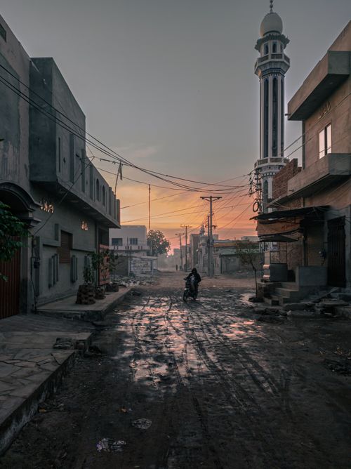 Free Dawn breaks over a street in Faisalabad, Pakistan, featuring a prominent minaret and a lone scooter rider. Stock Photo