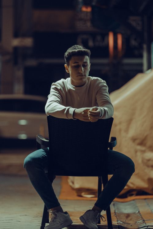 Free Young man in casual wear sits on a chair outdoors at night, exuding tranquility. Stock Photo