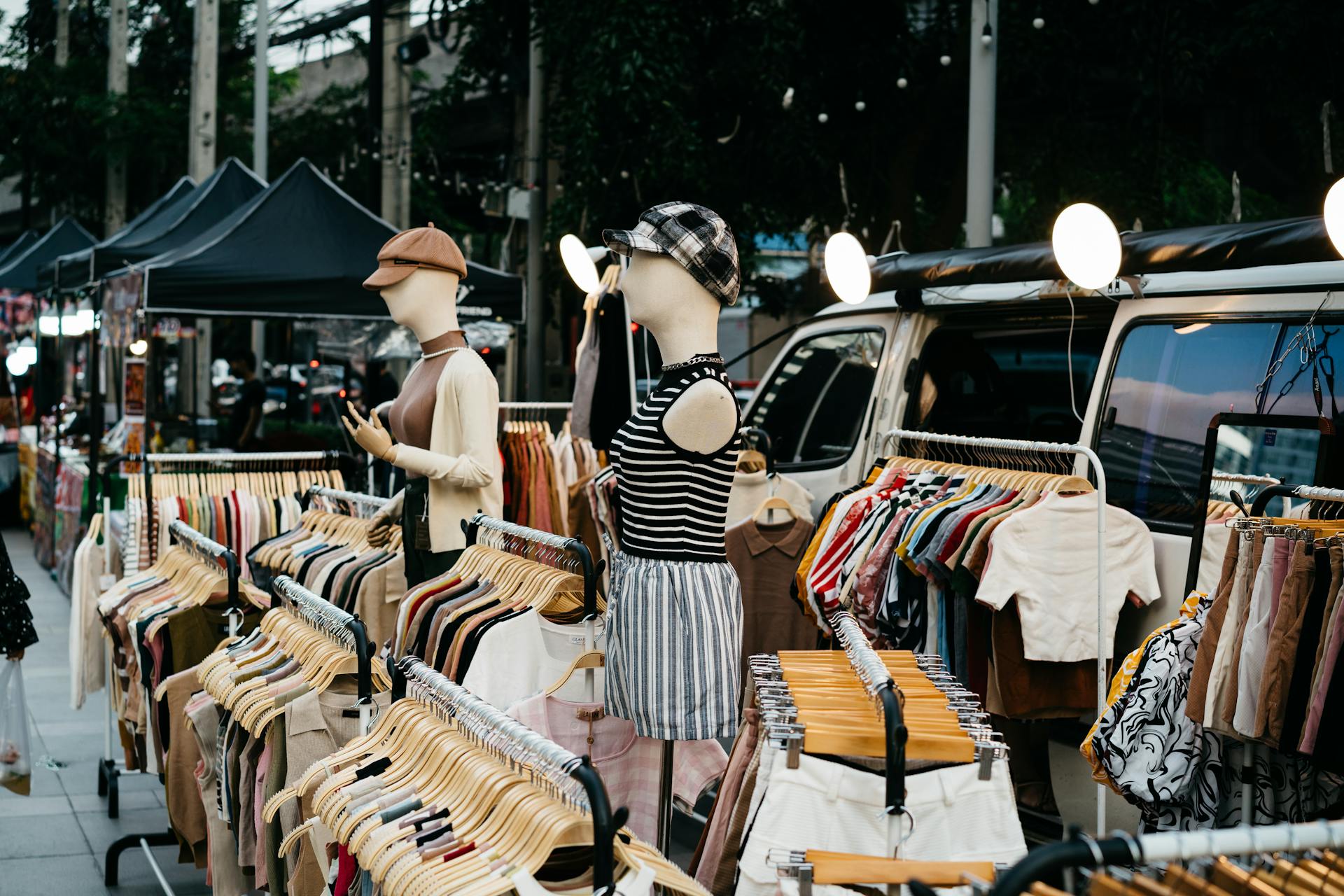A vibrant street market display featuring mannequins and clothes on racks under tents.