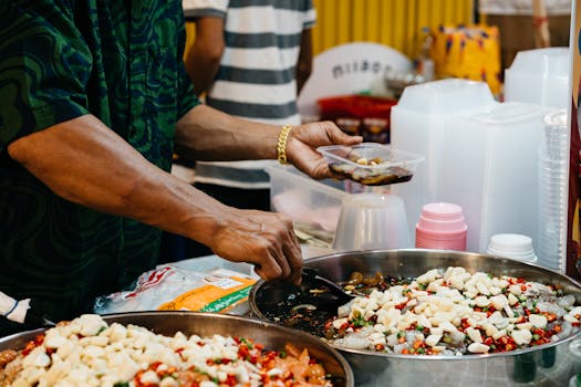 Close-up of a street food vendor serving a spicy dish with hands at a bustling market.