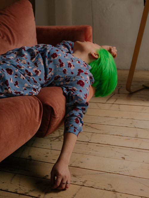 Free A woman with vibrant green hair lying on a pink couch in a fashion-forward indoor setting. Stock Photo