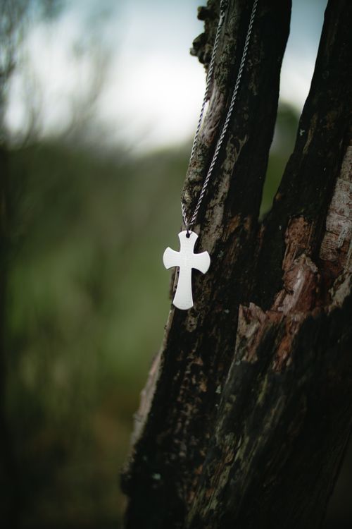 Free A close-up of a cross necklace hanging on a tree trunk outdoors, symbolizing faith. Stock Photo