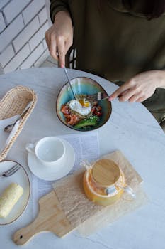 A woman enjoys a healthy breakfast with a poached egg and salad, paired with a cup of tea.