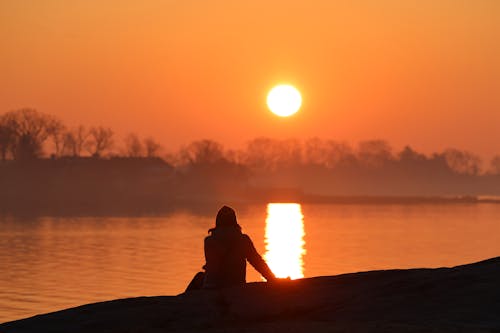 Woman Sitting on the Lakeshore and Looking at Sunset 