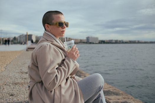 Young Woman Sitting on the Seashore Drinking Coffee