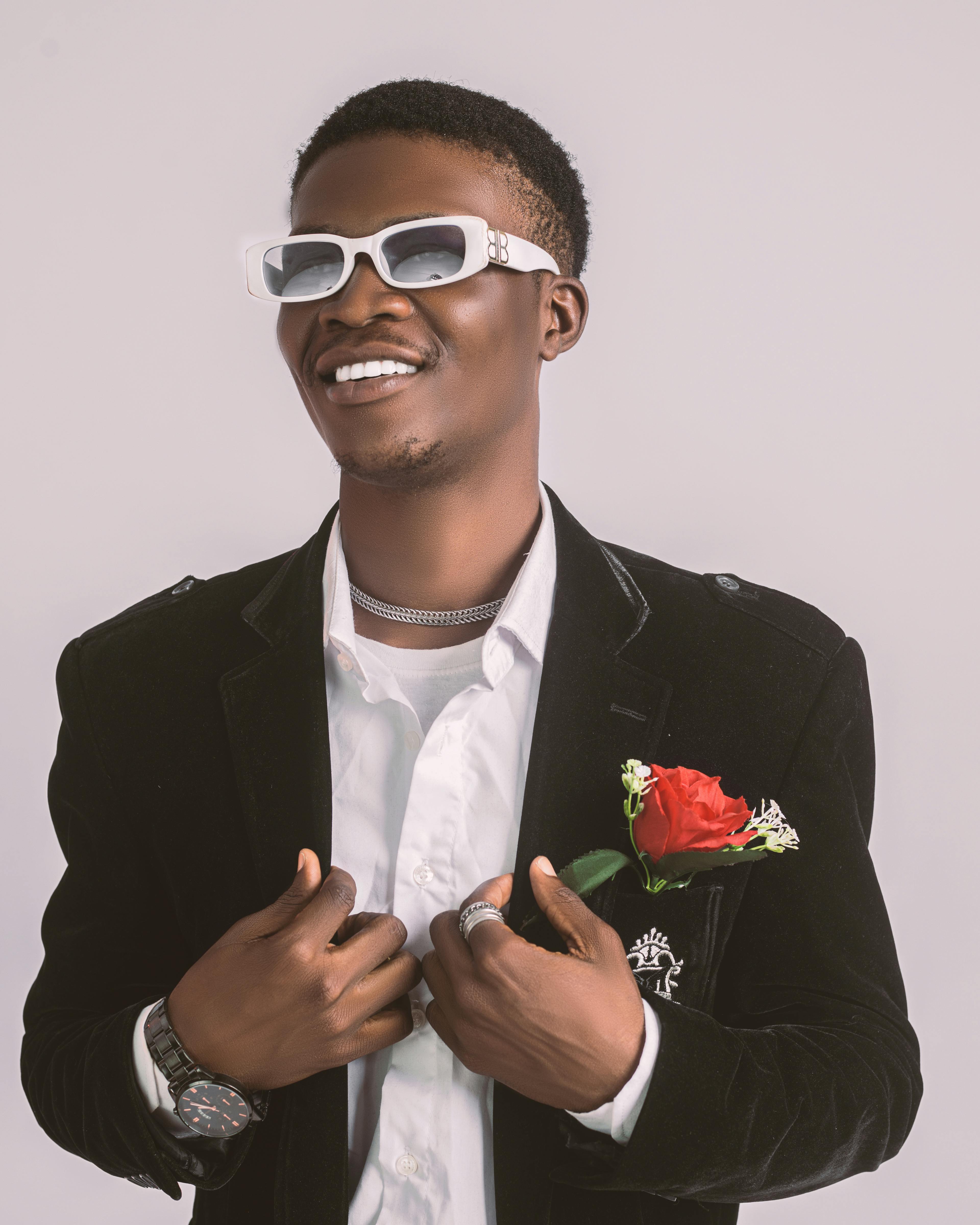 Fashionable man in a black blazer and sunglasses holding a red rose, showcasing modern style.
