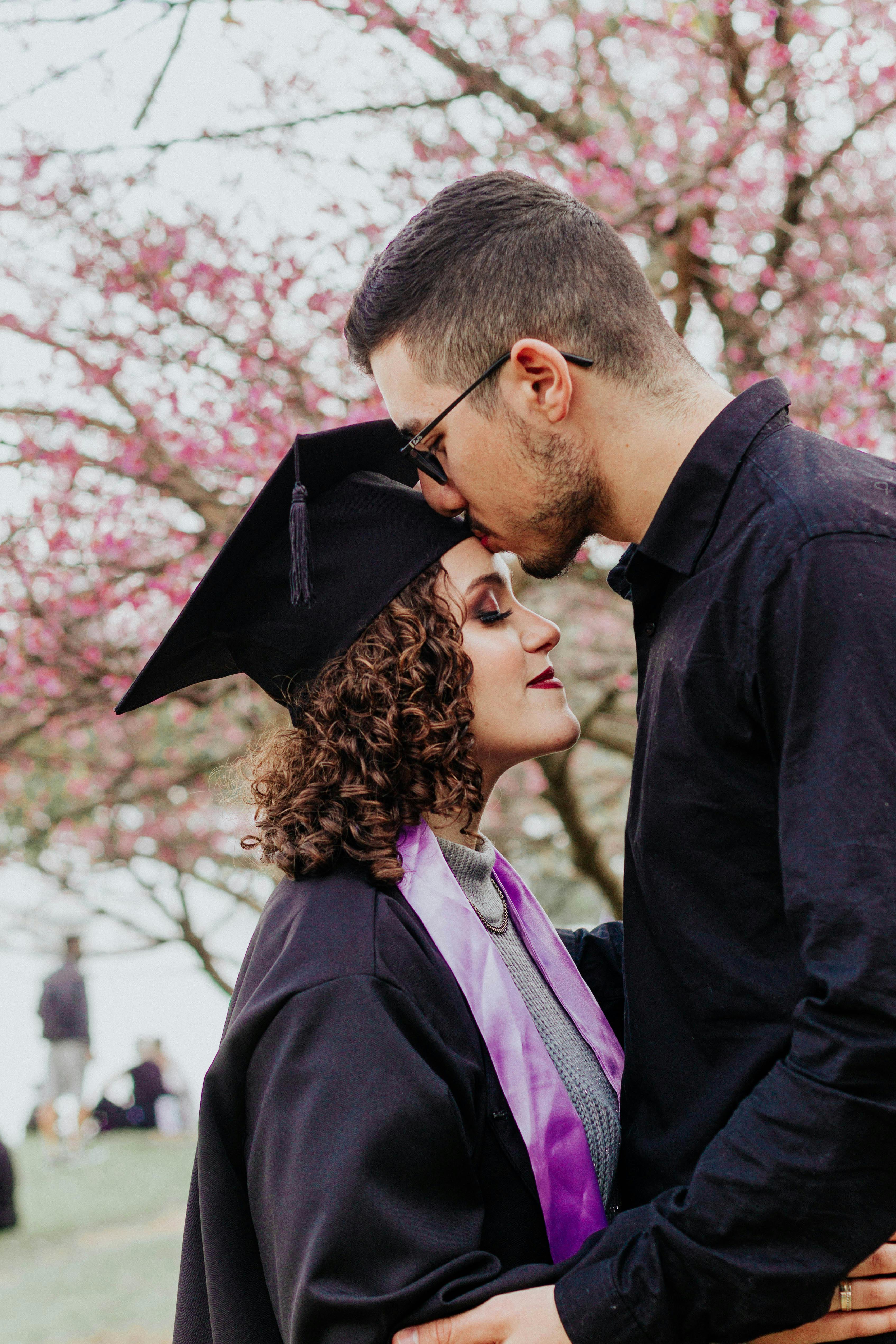 A couple shares an intimate moment under cherry blossoms on graduation day.