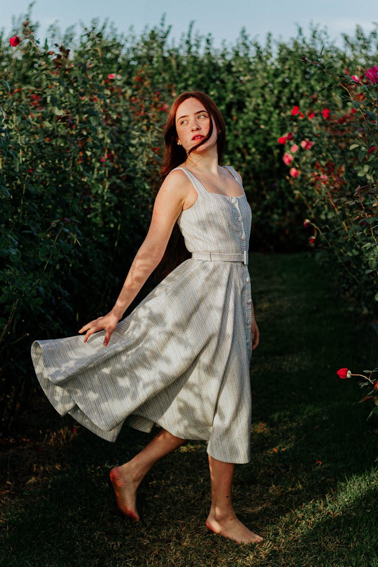 Young Woman In A Dress Walking Barefoot On The Grass