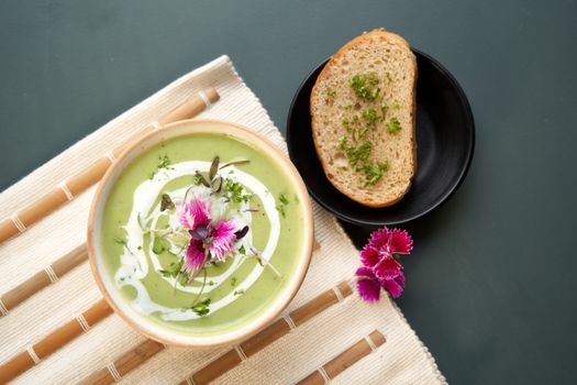 Top view of green creamy soup with floral garnish and bread slice, perfect for healthy dinner inspiration.