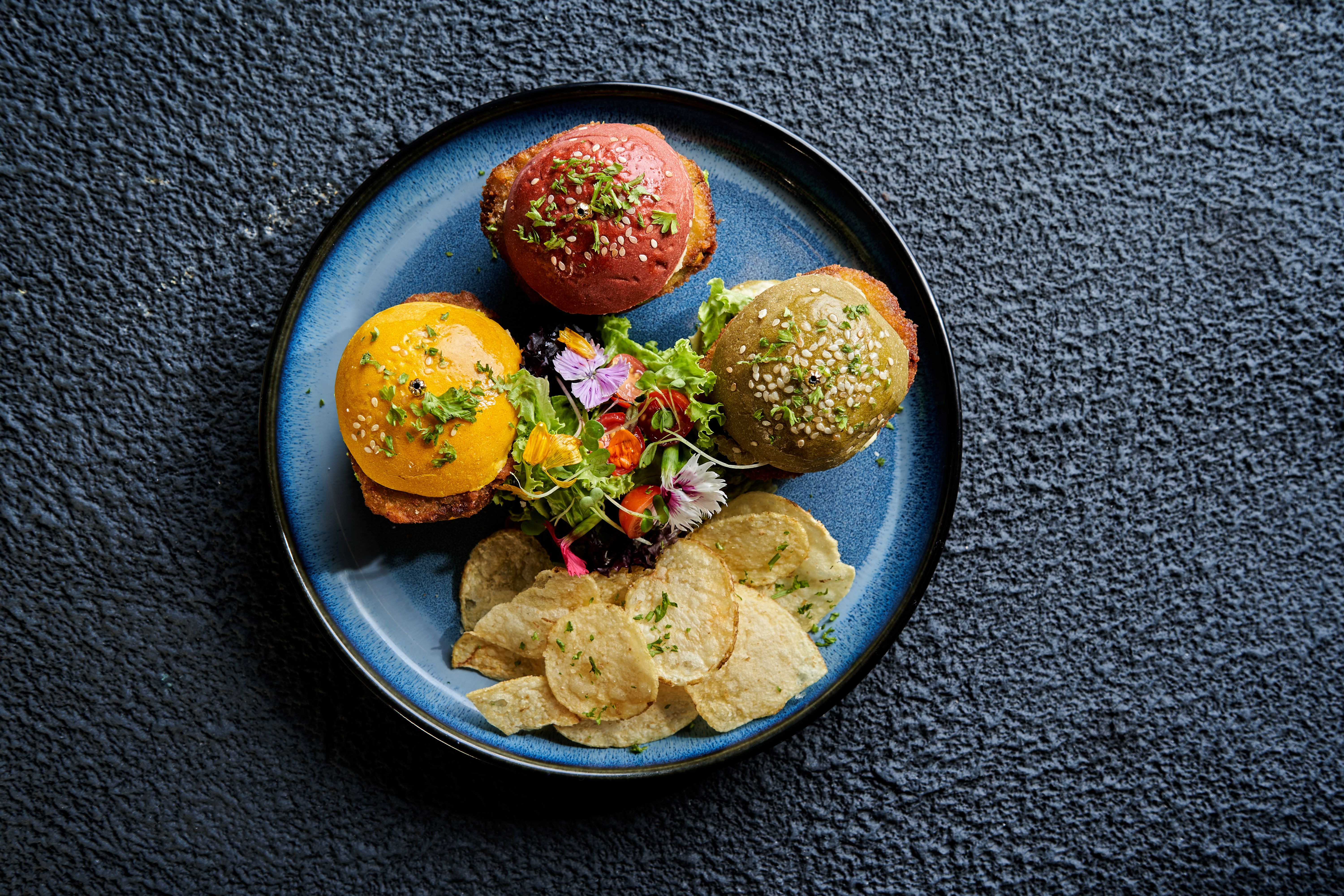Top view of colorful mini burgers with chips and salad on a plate.